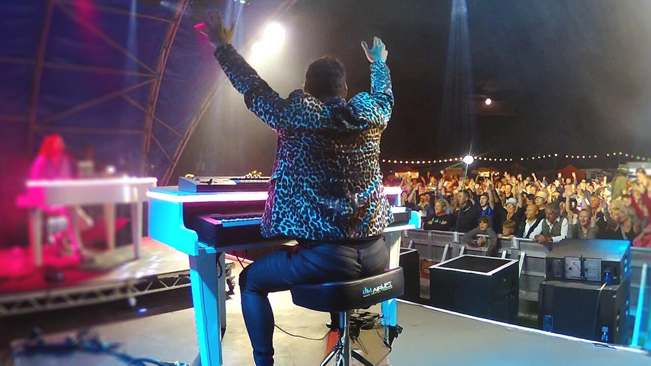 Large audience singing along during a duelling pianos performance with live band on stage