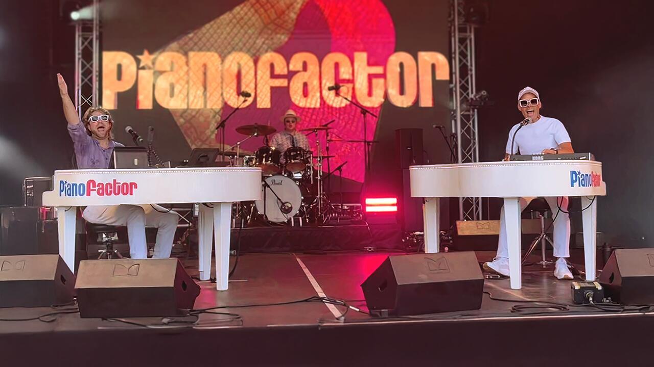 Audience gathered around duelling pianos performers singing along during a live music performance