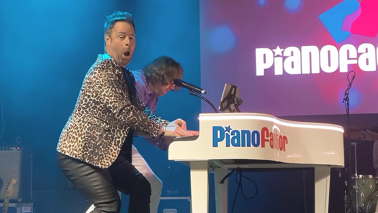 Two performers playing the same piano together during a duelling pianos performance
