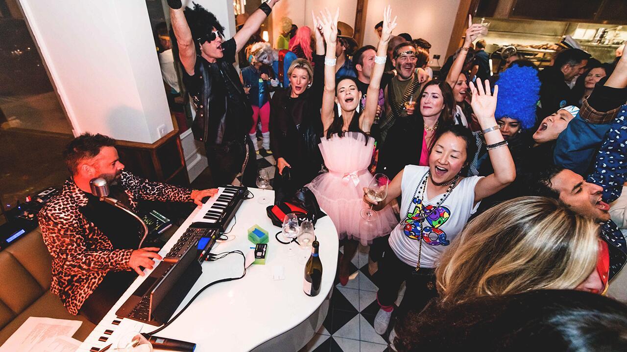 Piano entertainer performing in a pop-up piano bar setup with guests gathered nearby