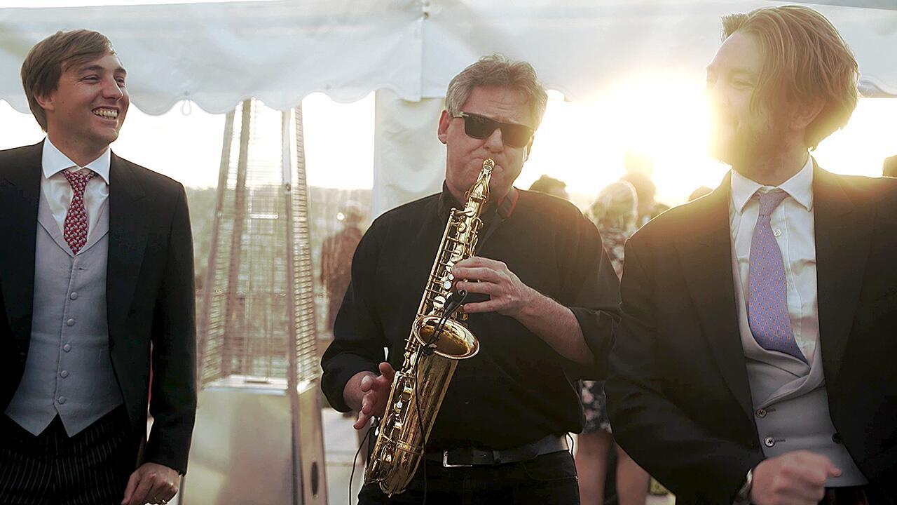 Wedding guests gathered around a saxophonist playing during a reception